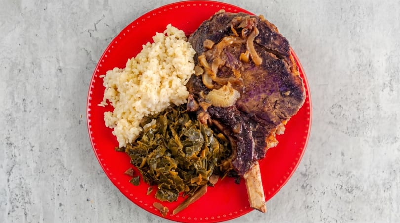 Braised short rib with onions, rice, and collard greens on a red plate.