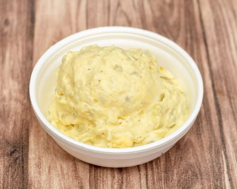 Creamy potato salad with visible herbs and spices in a white bowl on a wooden surface.