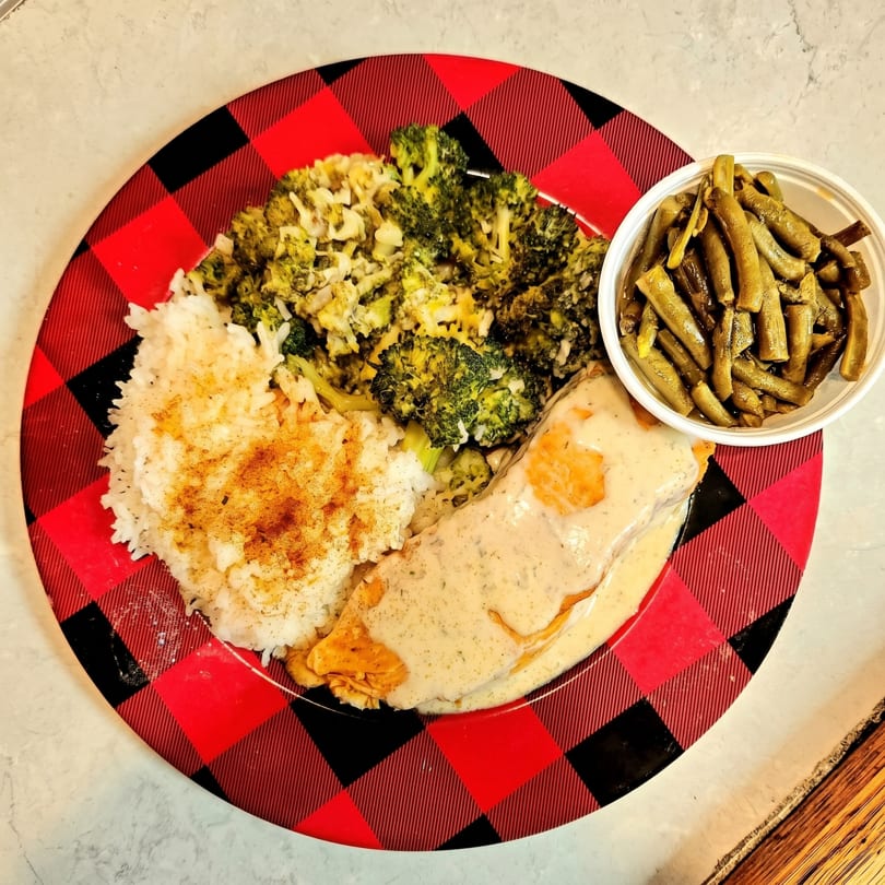 Chicken with cream sauce, rice, broccoli, and green beans on a red and black plaid plate.