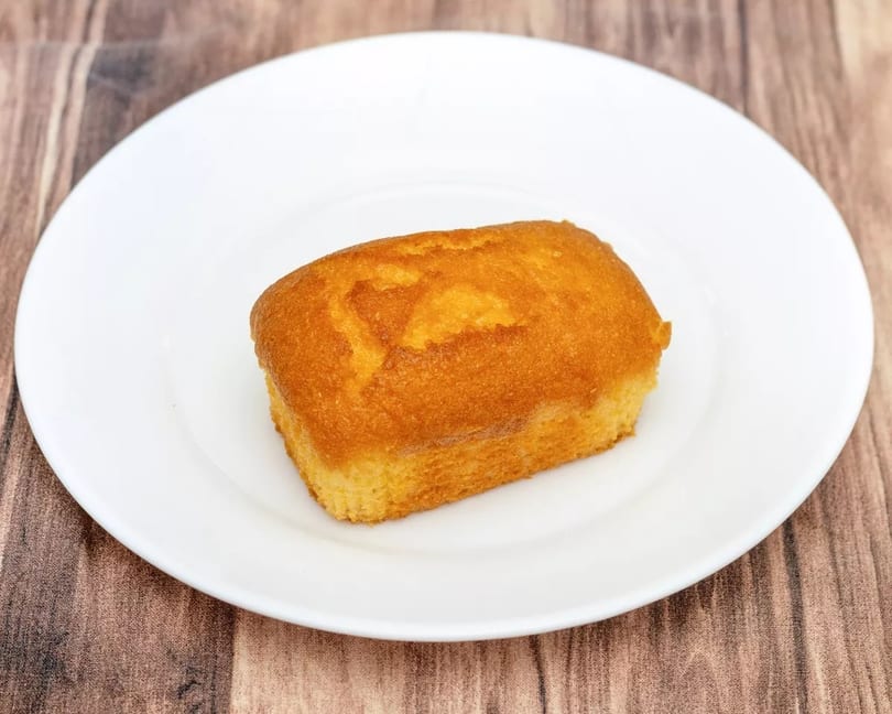 Golden brown pound cake on a white plate, set against a rustic wooden background.