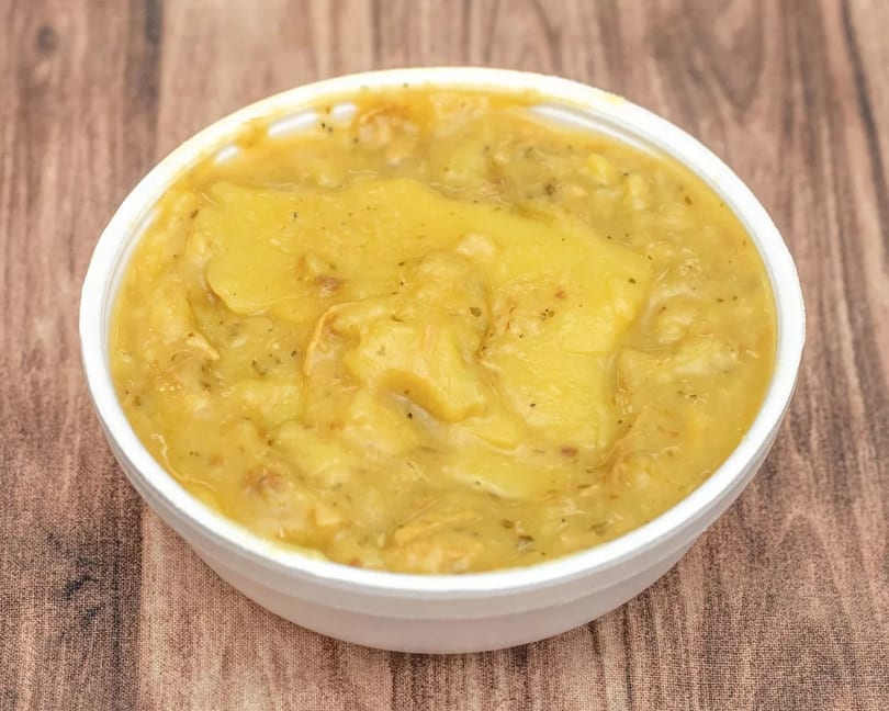 A white bowl filled with a thick, yellow potato soup, garnished with herbs, on a wooden surface.
