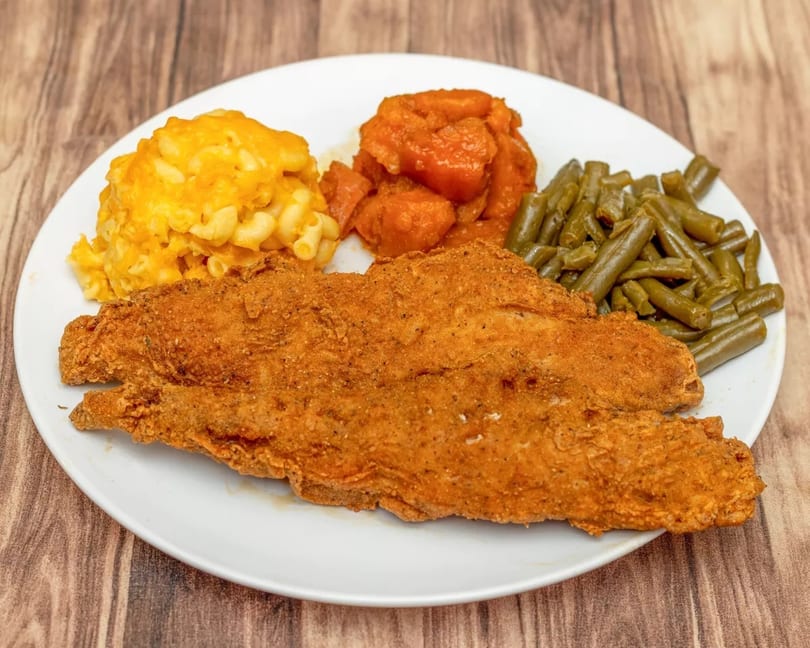 Fried fish fillets with macaroni and cheese, candied yams, and green beans on a white plate.