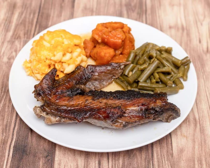 Smoked ribs, macaroni and cheese, candied yams, and green beans on a white plate.
